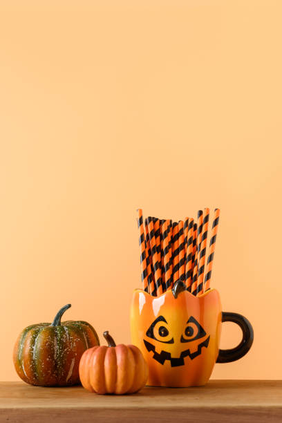 istock Halloween fun party decorations, candy bowl, pumpkins, sweets, mug with drinking straw on orange. Vertical composition. 1336486612