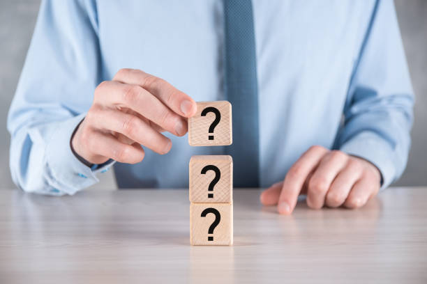 istock Businessman hold and put wooden cube block shape with question marks on grey table. Space for text.concept for confusion, question or solution 1336489558