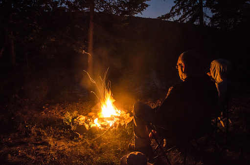 Woman and man sitting in front of campfire during summer night