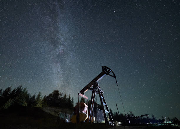 Oil pump jack at night time under starry sky. Pumpjack against starry sky with Milky way in natural mountains environment for mining gasoline, pipeline system extract crude oil petroleum and water emulsion at each stroke during night time oil wellhead stock pictures, royalty-free photos & images