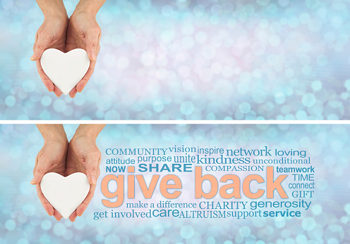 female hands holding a white heart beside a GIVE BACK word cloud against a pale blue grey bokeh background