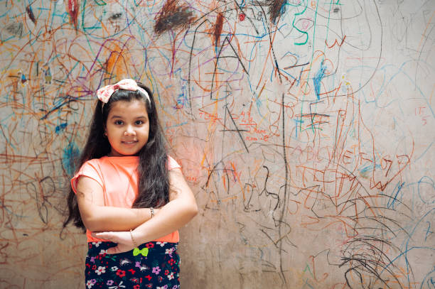 自宅で壁にマーカーで描く面白いかわいい女の子。リビングルームの壁に若いアーティストの絵画 - schoolgirl little girls crayon human face ストックフォトと画像