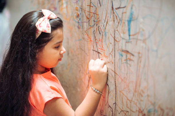 divertida niña linda dibujando con marcador en la pared en casa. joven artista pintando en la pared de la sala de estar - schoolgirl little girls crayon human face fotografías e imágenes de stock