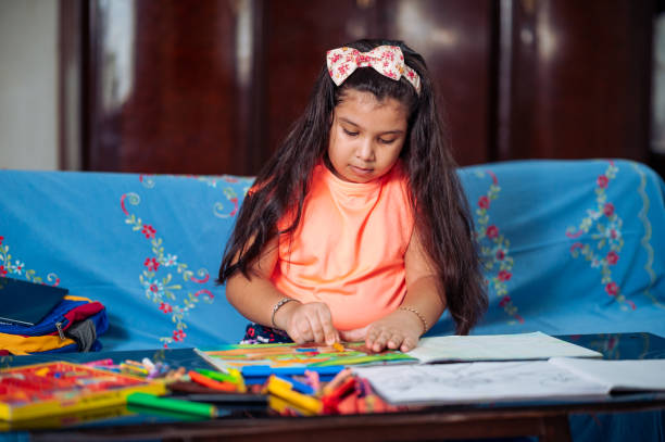 linda niña estudiando en casa, haciendo dibujo o proyecto de arte con colores y crayones mientras está sentada en el sofá. - schoolgirl little girls crayon human face fotografías e imágenes de stock