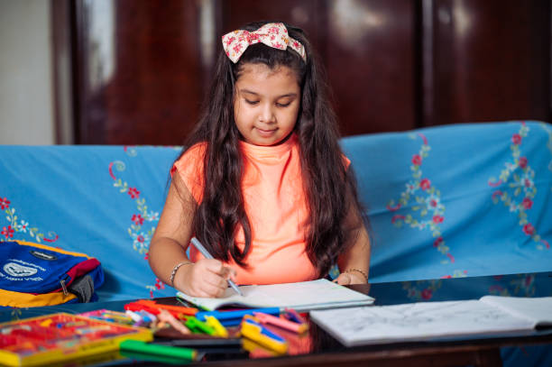 linda niña estudiando en casa, haciendo dibujo o proyecto de arte con colores y crayones mientras está sentada en el sofá. - schoolgirl little girls crayon human face fotografías e imágenes de stock