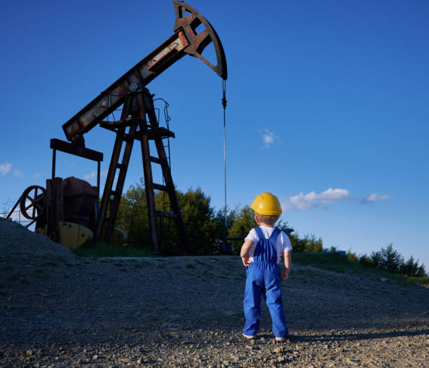 Child studying business development at oil station Back view of intelligent child studying business development at oil station with mining platform and drilling rig, boy in yellow helmet and blue uniform for kids looking at machine construction oil pump petroleum equipment development stock pictures, royalty-free photos & images