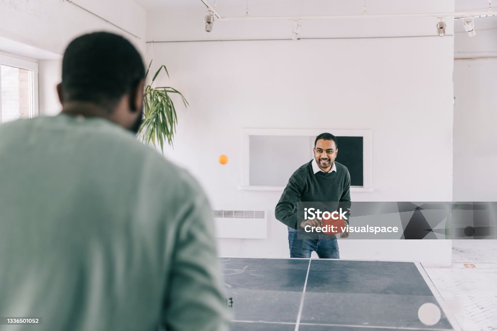 Taking time off at the office Colleagues playing table tennis at creative office space. Table Tennis Stock Photo