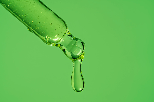 A drop of serum from a pipette. On a bright green background.