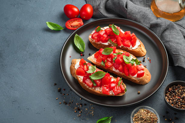 istock Three bruschetta with tomatoes, basil and cheese on a black plate 1336505984