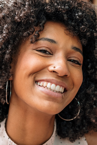 Portrait of a beautiful friendly smiling Black woman with curly hair and nose and lip piercings looking at the camera with laughing eyes in a close up cropped view
