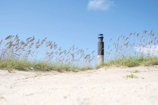 Scenic coastal landscape with lighthouse in background behind sand dunes and grasses in early morning