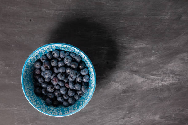istock Blueberries in blue bowl on dark grey background. Flatlay. 1336509423