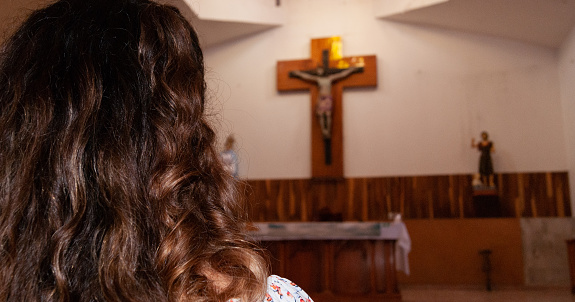 over shoulder woman with her back facing the altar with the cross of Christ in the background