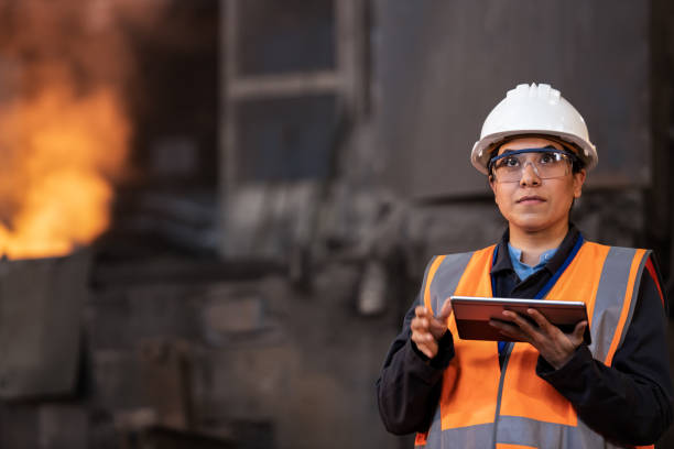 vue de face d’une femme portant un équipement de sécurité et observant les processus logistiques dans une grande usine sidérurgique - aciériste photos et images de collection