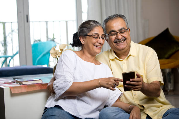 Old couple enjoying using mobile phone at home stock photo