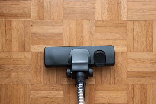 Vacuum cleaner attachment on wooden floor tiles inside room, no people, top view.
