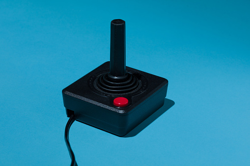 Vintage arcade game joystick with red buton on blue background.