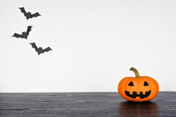 istock Halloween jack o lantern on a black shelf against a white wall with bats 1336521948