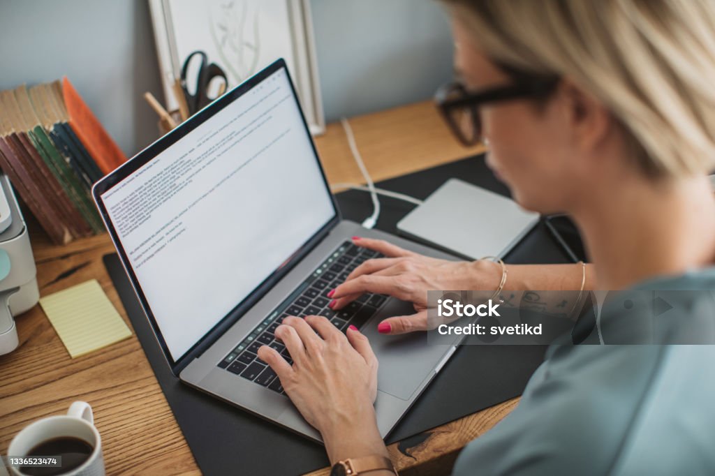 Young book author Young book author writing book at home. She is sitting at the desk and using laptop for writing. Publisher Stock Photo