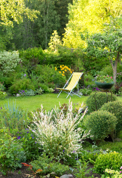 piękny ogród kwiatowy z zielonym trawnikiem i żółtym krzesłem ogrodowym na nim latem, pionowo - deck chair summer grass outdoor chair zdjęcia i obrazy z banku zdjęć