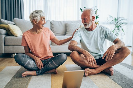 Beautiful mature couple sitting on the floor and practicing yoga. Sporty couple using digital tablet for online yoga lessons.