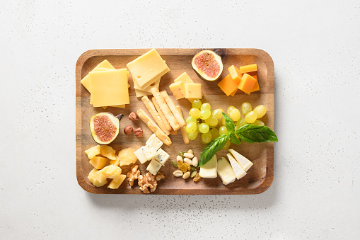 Cheese platter with grapes, nuts, figs on a white background. View from above. Festive gourmet snack.