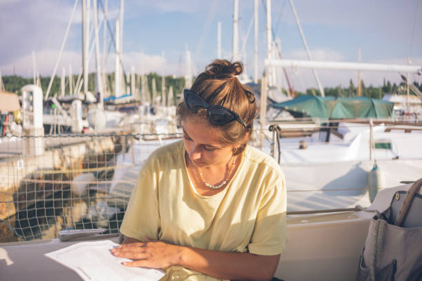 Young woman reads on a sailboat in a marina View from sailboat, in summer sailboat mast stock pictures, royalty-free photos & images