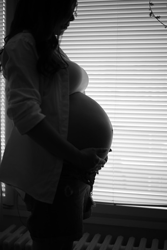 Photo of a young expectant mother stroking her baby bump and enjoying her morning in the bedroom of her apartment; the daily routine of a pregnant woman.