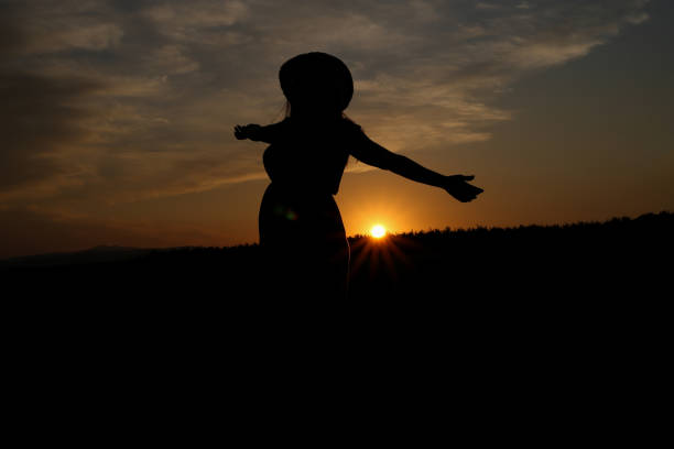 A man stands in silhouette against the backdrop of a glowing sunrise over rugged mountain ranges. The warm hues of dawn illuminate the horizon, creating a serene and contemplative moment. Perfect for themes of adventure, mindfulness, solitude, nature exploration, and scenic travel.