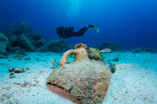 An ancient, Greek Amphora with a scuba diver silhouette behind