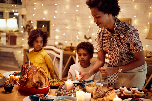 Single black mother celebrating Thanksgiving with her children and lights candles during dinner at dining table.