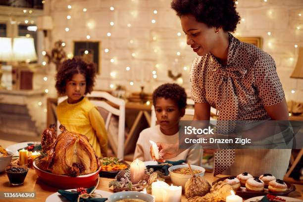 African American Mother Lights Candles During Thanksgiving Meal At Dining Table Stock Photo - Download Image Now