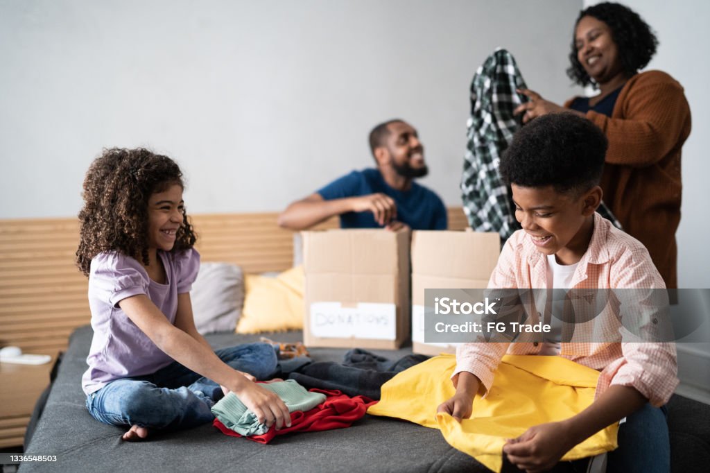 Parents with children sorting out clothes in boxes to donate at home Decluttering Stock Photo