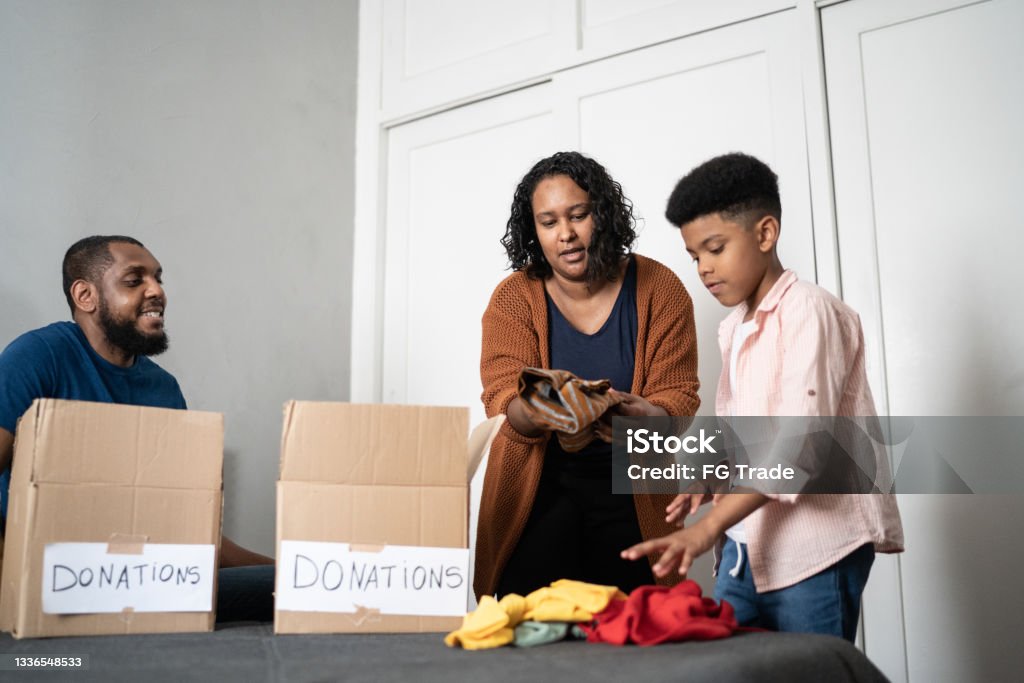 Parents with son sorting out clothes in boxes to donate at home Decluttering Stock Photo
