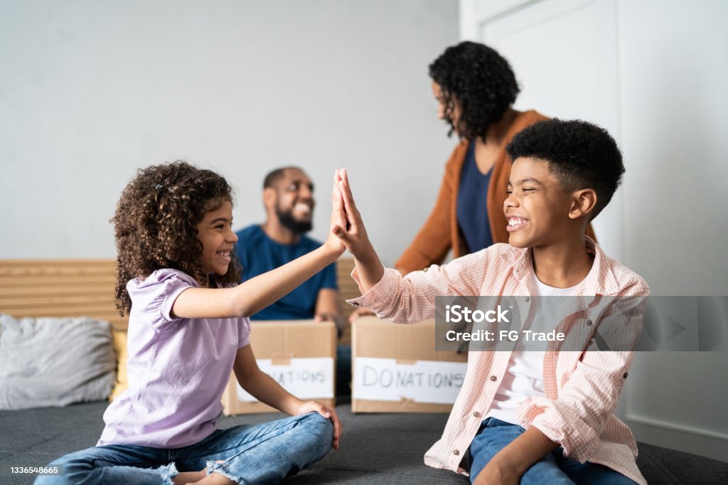 Siblings doing high five while sorting out clothes for donation Child Stock Photo