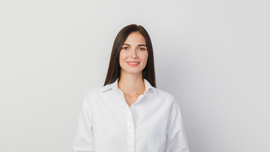 A young woman portrait on a solid white background. A woman with a charming smile. A woman in a white shirt poses in the studio