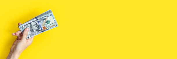 istock Hand holding a big stack of banknotes isolated on yellow background. Wealth or loan concept. Long Banner with copy space 1336552019