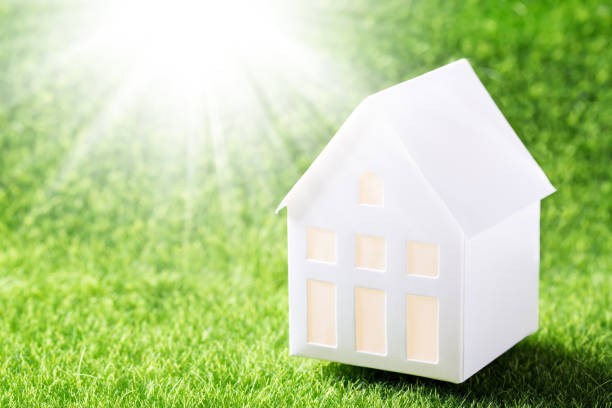 istock Model of white paper house on green grass background 1336553375