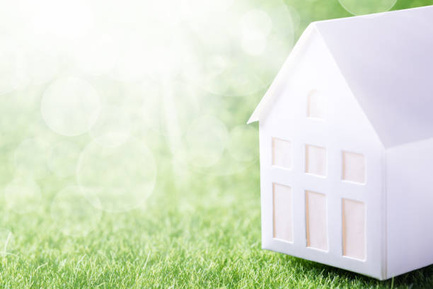 istock Model of white paper house on green grass background 1336553390