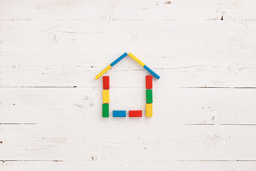 Colored wooden cubes assembled in the shape of a house on a white wooden background. Early development for children. Home, family and education concept.