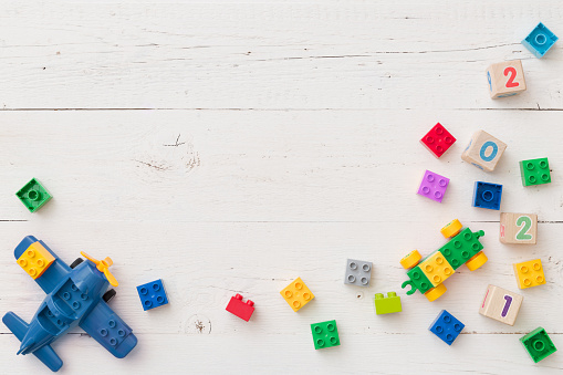 Close up of wooden cubes with numbers of year 2021 and other numbers. Top view of children's educational toys, blue plane, colorful cubes, bricks on a white wooden background.
