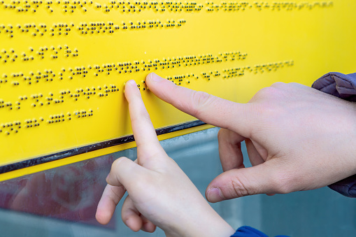 A blind person reads a Cyrillic Braille text and teaches a child how to read it.