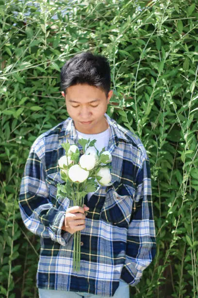 Photo of young men holding of white rose flowers at park garden