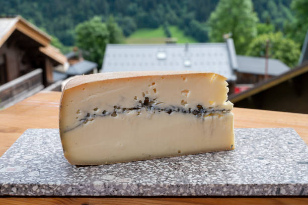 käsesammlung, französischer käse aus roher kuhmilch morbier und französisches bergdorf in haute-savoie im hintergrund - morbier stock-fotos und bilder