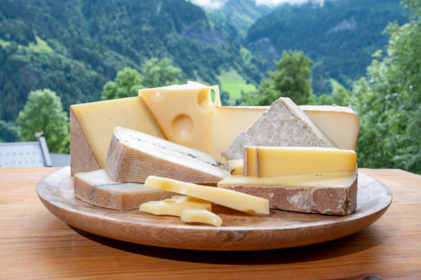 cheese collection, wooden board with french cheeses comte, beaufort, abondance, emmental, morbier and french mountains village in haute-savoie on background - morbier imagens e fotografias de stock