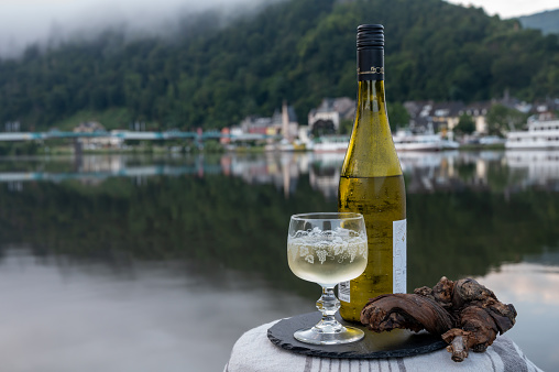 Tasting of white quality riesling wine served on outdoor terrace in Mosel wine region with Mosel river and old German town on background, Germany