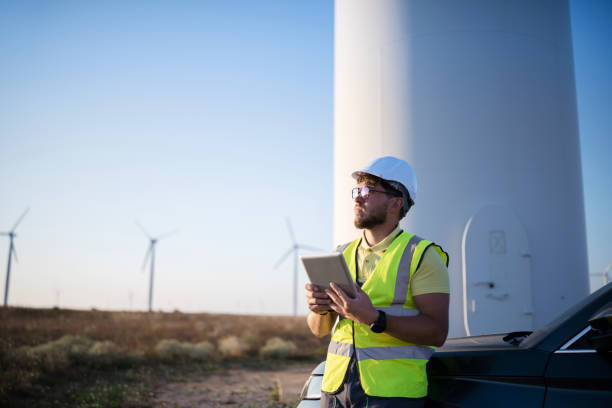 joven ingeniero buscando y comprobando turbinas eólicas en el campo usando una tableta digital - accesorio de cabeza fotos fotografías e imágenes de stock