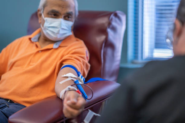 masked senior man donating blood at a medical clinic - bloedbank stockfoto's en -beelden