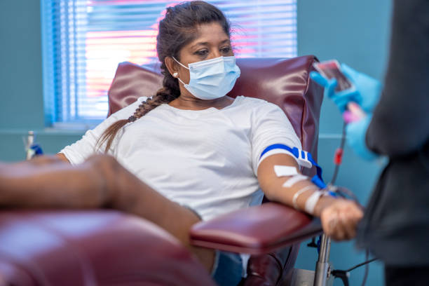 masked female adult donating blood at a clinic - bloedbank stockfoto's en -beelden