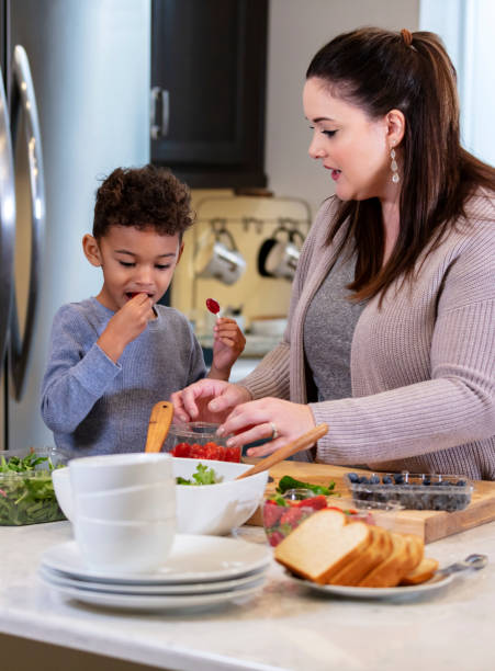 istock Mother in kitchen making salad, son eating tomato 1336579058